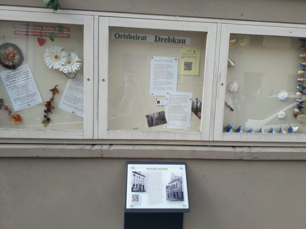 Das Bild zeigt ein Schwarzes Brett mit Informationen zu Vereinen und Begegnungsmöglichkeiten in Drebkau. Vor dem Brett ist eine historische Schautafel angebracht, die über den Ort und seine Geschichte informiert.